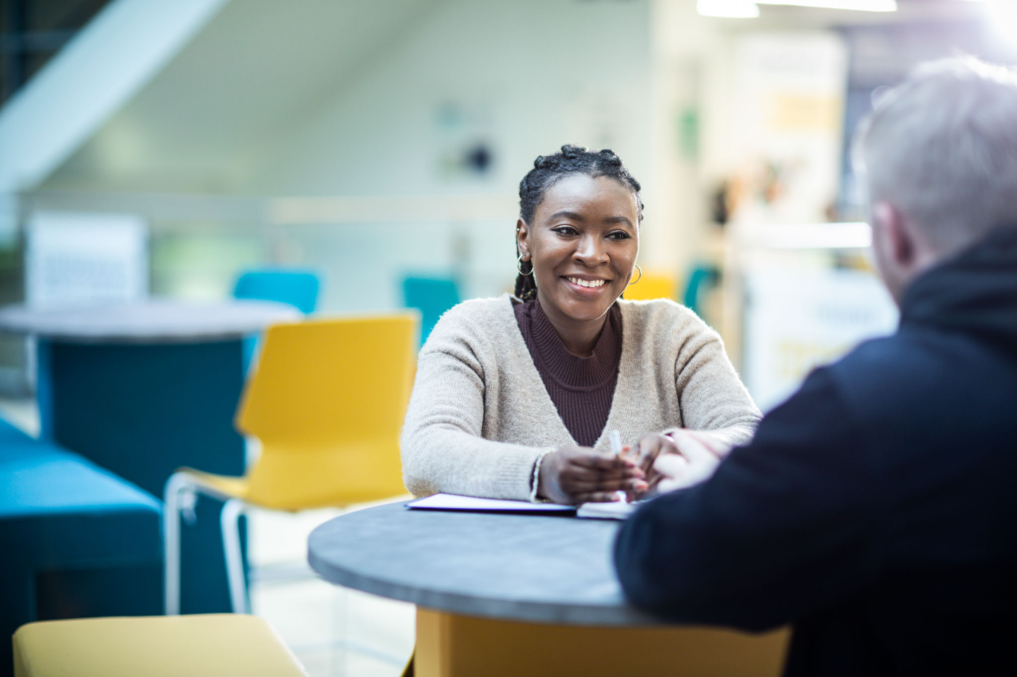 Postgraduate student sitting at table smiling and chatting with a member of staff